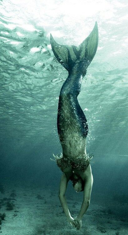 A mermaid with green tail swims downwards underwater with light shining from above.